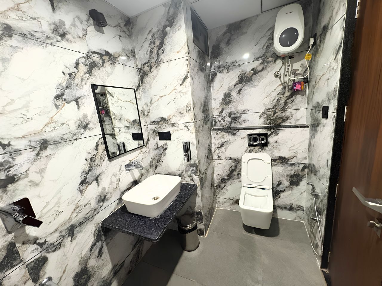 A bathroom with a marble wall, a sink, a toilet, and a mirror.