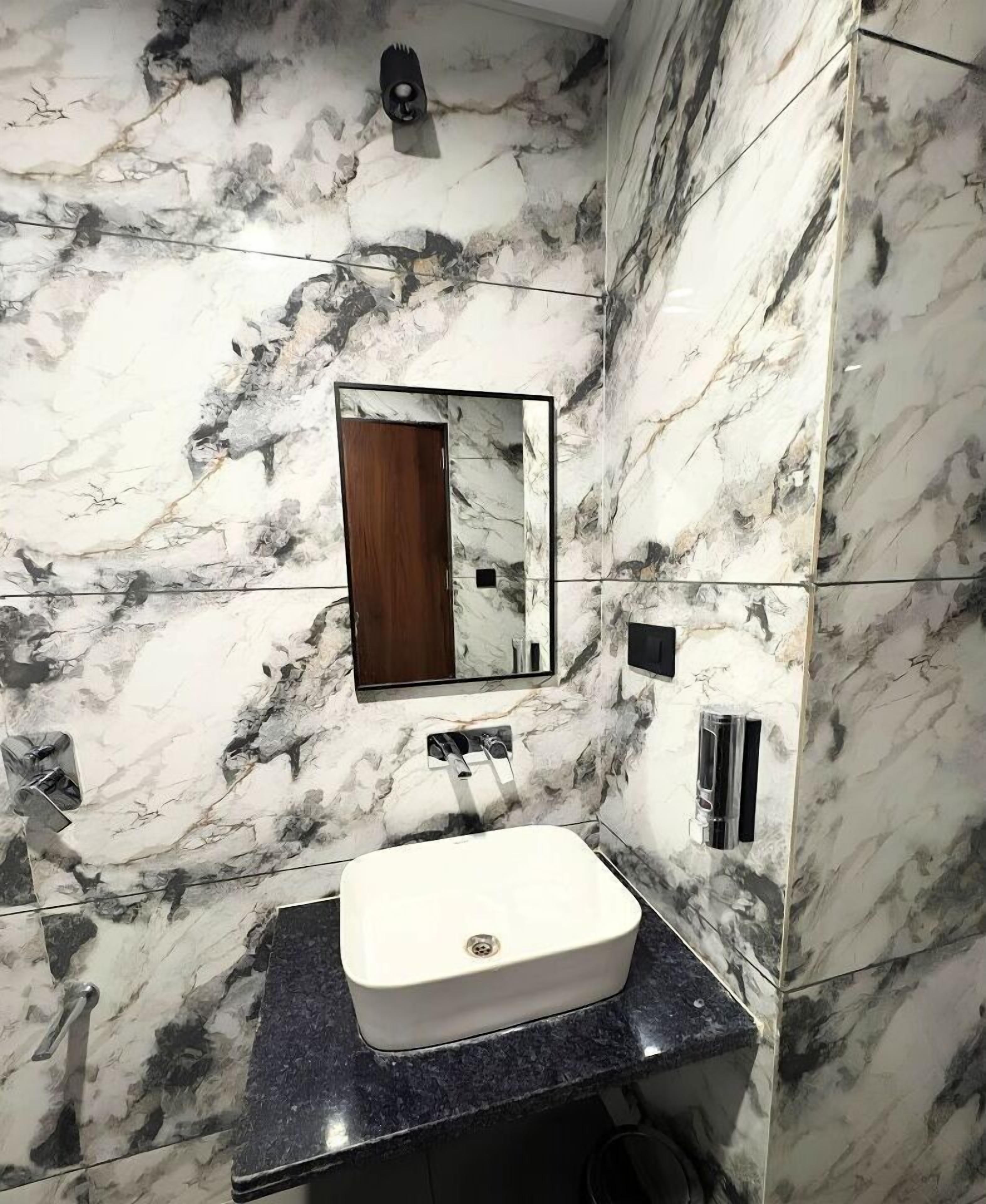 A bathroom with a marble wall, a sink, a mirror, and a shower area.