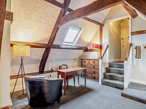 A loft bedroom with exposed wooden beams, a desk, a chair, a dresser, and a staircase. - Manor View First Floor Apartment - UK39044 (Peterstow)