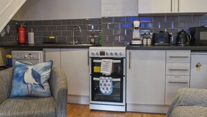 A modern kitchen with white cabinets, a stove, oven, and a microwave. There is a clock on the wall and a fire extinguisher on the counter. - 2 bedroom accommodation in Looe (Looe)