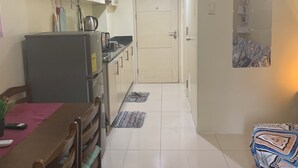 A compact kitchen with a refrigerator, stove, and cabinets. There is a dining table with chairs and a patterned rug. A door leads to another room. - Tranquil 1-bedroom condo with AC in Pasay City (Pasay City)