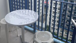 A balcony with a round table and two plastic stools. The balcony has a blue railing. In the background, there are multi-story buildings with balconies. - Tranquil 1-bedroom condo with AC in Pasay City (Pasay City)