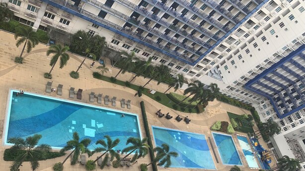 A high-rise building with multiple balconies, a swimming pool, and palm trees. - Tranquil 1-bedroom condo with AC in Pasay City (Pasay City)