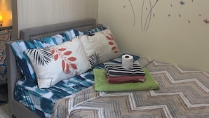 A neatly made bed with patterned bedding, a wall decoration with flowers and butterflies, and a bedside table with a lamp. - Tranquil 1-bedroom condo with AC in Pasay City (Pasay City)