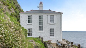 A white building with multiple windows and a chimney, situated by a body of water. - 2 bedroom accommodation in Beesands (Beesands)