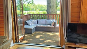 A cozy room with a wooden interior, a sliding glass door leading to an outdoor seating area with a wicker sofa and cushions, a flat-screen TV, and a wooden coffee table. - 4 bedroom accommodation in Kenwick, near Louth (Kenwick, near Louth)