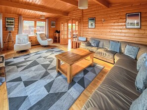 Ein gemütliches Blockhaus-Interieur mit einer Couch, einem Holztisch und einem gemusterten Teppich.