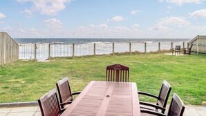 Eine Terrasse mit Tisch und Stühlen mit Blick auf den Ozean, mit Holzzaun und Sitzgelegenheiten an der Seite.