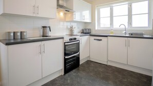 Eine moderne Küche mit weißen Schränken, einem schwarzen Backofen, einem Edelstahl-Wasserkocher und einem Fenster mit Aussicht.