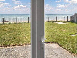 Une vue à travers une porte donnant sur un espace verdoyant, avec une clôture et une plage en arrière-plan.