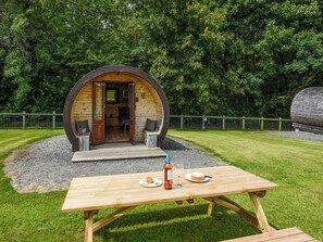 Eine rustikale Holzkonstruktion mit einer Rundtür, zwei Sitzbereichen und einem Picknicktisch mit Speisen und Getränken.
