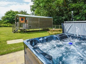 A hot tub with water jets, a wooden deck, and a small wooden structure with a porch. - Bluebell - Shepherd Hut - UK49948 (Oswestry)