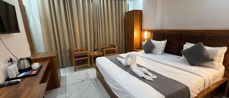 A hotel room with a large bed, a desk with a kettle, and a TV.