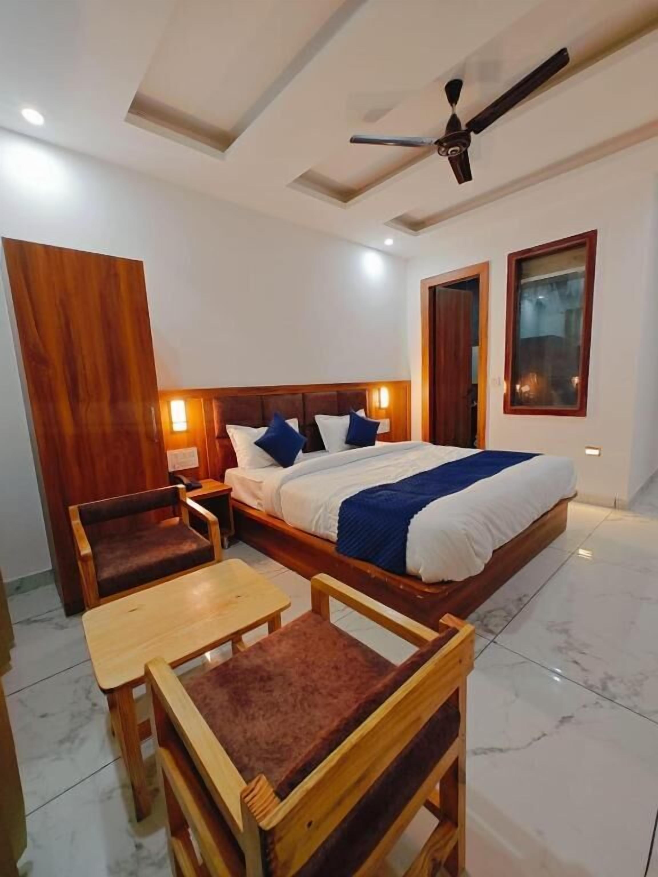 Habitación de hotel con una cama grande, cabecero de madera, dos mesitas de noche, ventilador de techo y ventana con vistas.