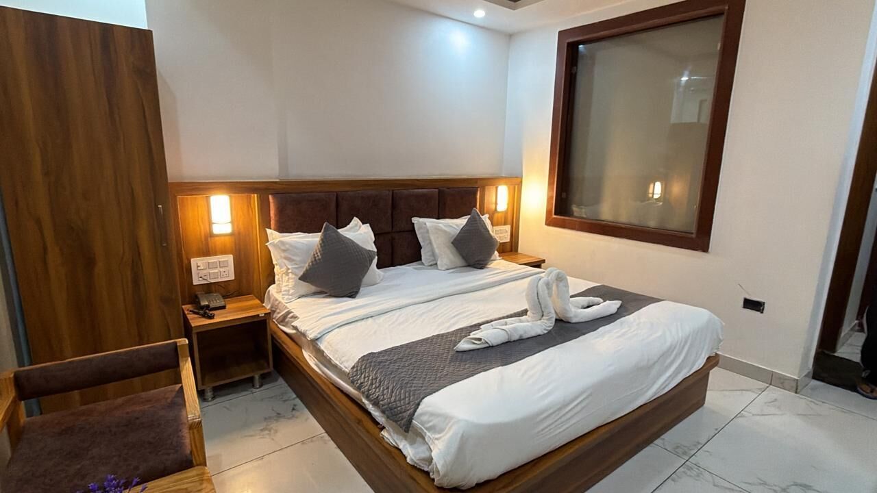 A hotel room with a large bed, wooden headboard, bedside tables with lamps, a wooden wardrobe, and a large window.