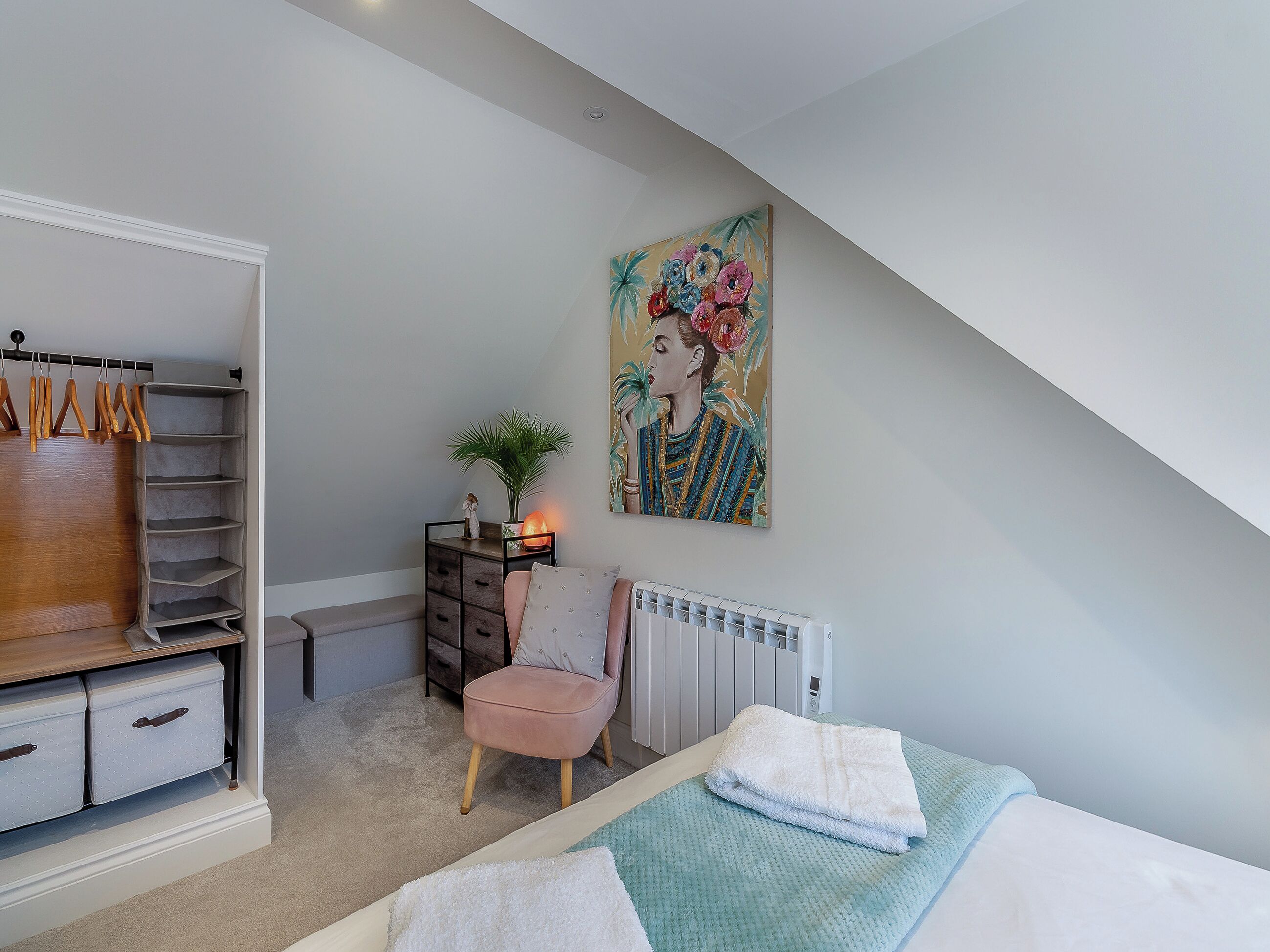 A bedroom with a bed, a chair, a radiator, a wardrobe, and a painting on the wall.
