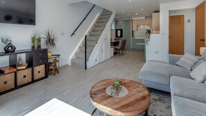 A modern living room with a grey sofa, a wooden coffee table, and a staircase leading to a dining area. - Olive Breeze is a bright spacious property in the old part of Felixstowe. (Felixstowe)