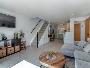 A modern living room with a grey sofa, a wooden coffee table, and a staircase leading to a dining area.