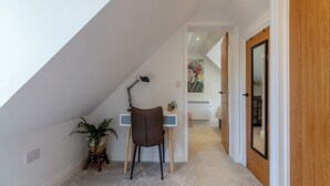Une petite pièce bien éclairée, avec un plafond en pente, un bureau avec une chaise, une plante en pot et un radiateur.