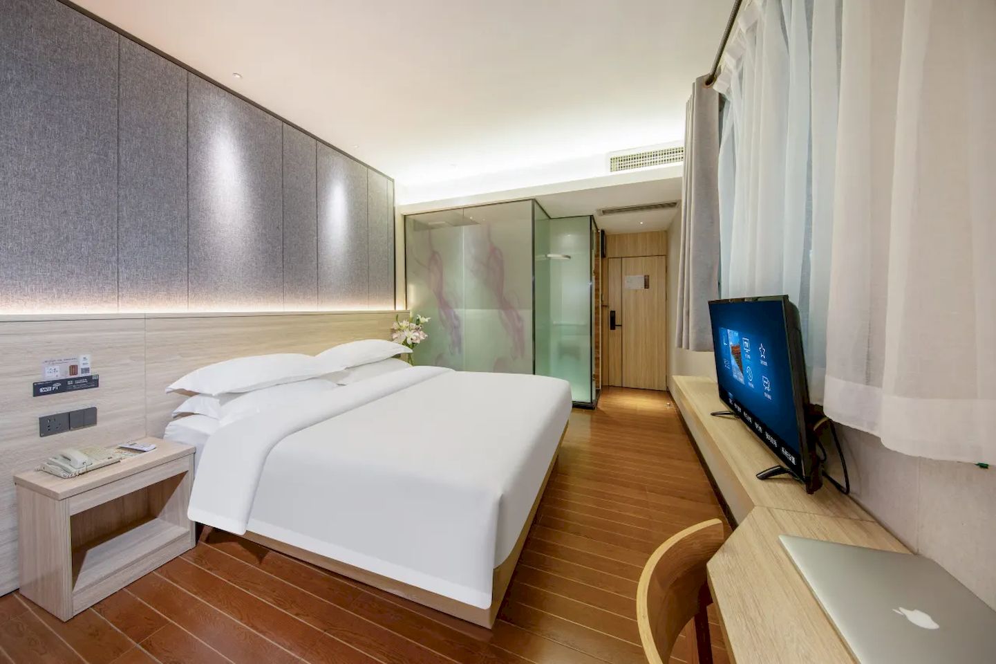 A hotel room with a bed, bedside table, TV, and a desk with a laptop.