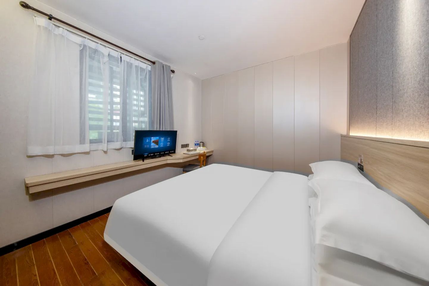 Ein Hotelzimmer mit einem Bett, einem Fernseher auf einem Tisch, einem Nachttisch aus Holz und einem Fenster mit Vorhängen.
