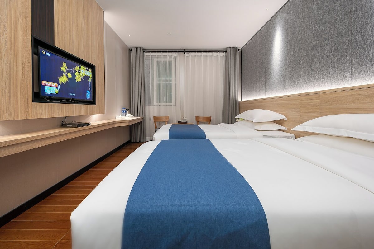 Une chambre d’hôtel avec un grand lit, un téléviseur fixé au mur, un bureau en bois et une fenêtre avec des rideaux.