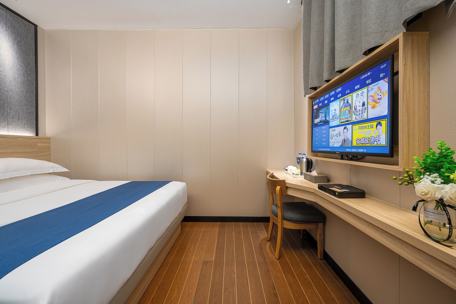 A hotel room with a bed, a desk, a chair, a television, and a small plant.