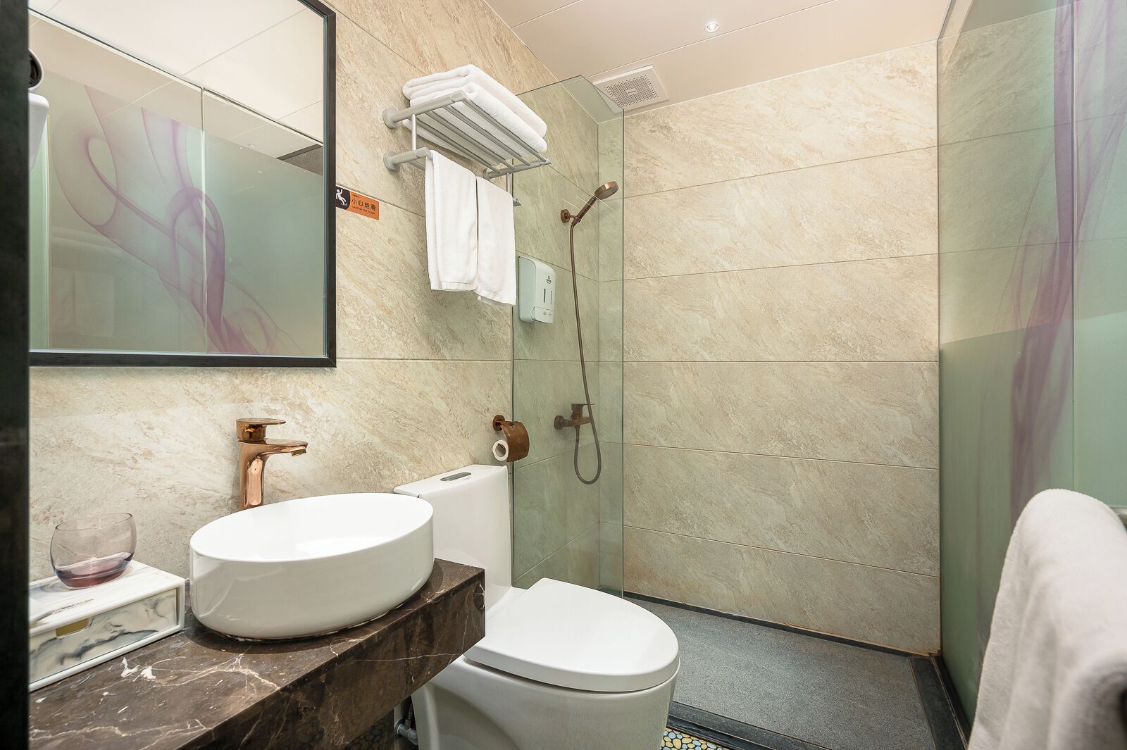A modern bathroom with a marble sink, a toilet, a glass shower enclosure, and a towel rack.