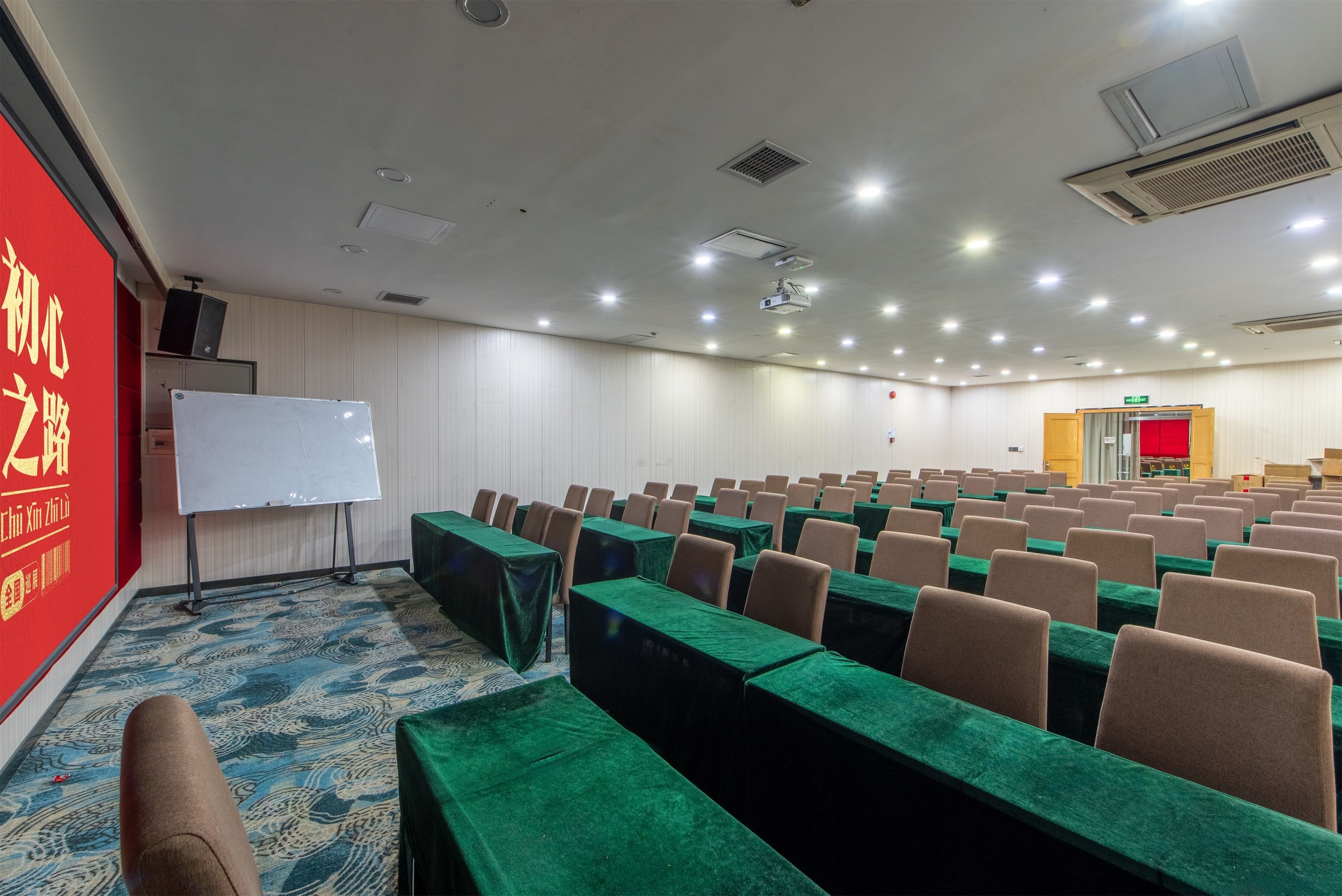 Une salle de conférence avec des rangées de tables et de chaises, un tableau blanc et un projecteur.
