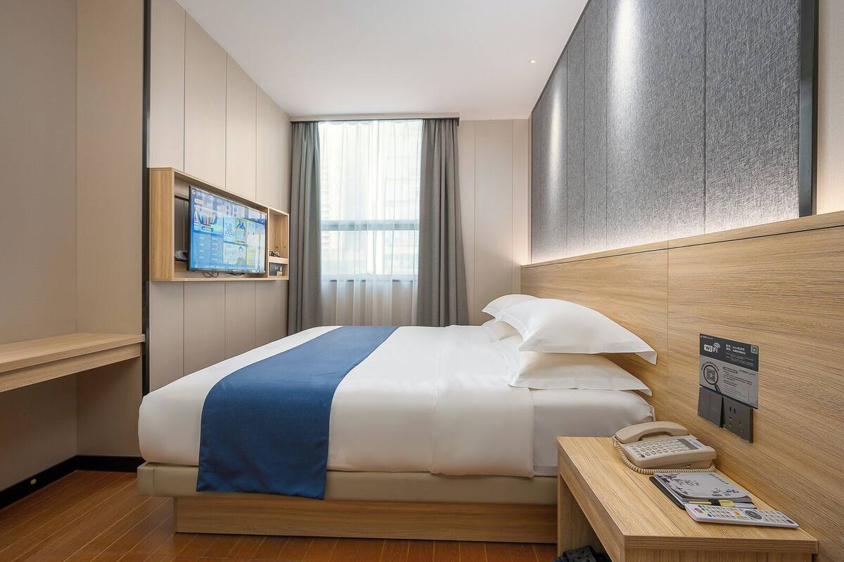 Une chambre d’hôtel comprenant un lit, un bureau avec un téléphone, un téléviseur fixé au mur et une fenêtre avec des rideaux.
