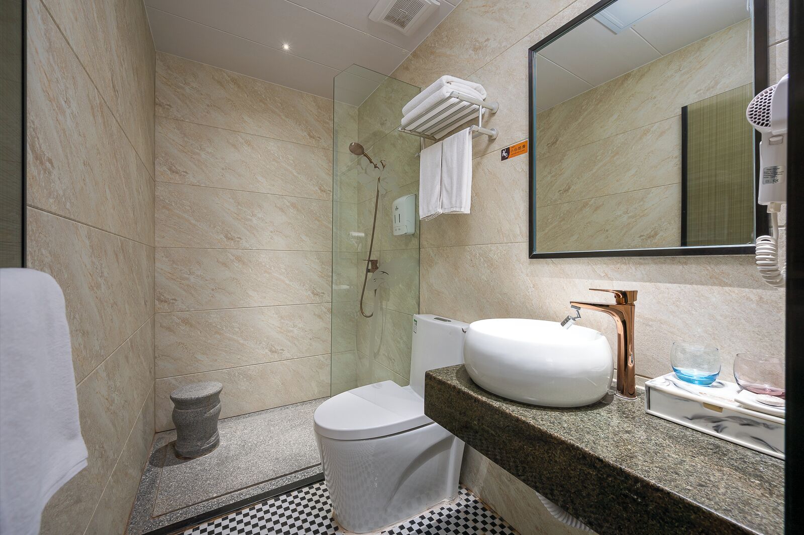 Un baño moderno con ducha envuelta en cristal, inodoro blanco y encimera de granito con lavabo y tocador.