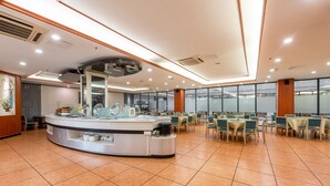Een modern restaurant met een centraal aanrecht, verschillende eettafels en een hoge plafond met inbouwverlichting.