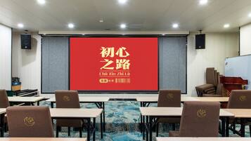 Un salón de conferencias con una pantalla roja mostrando caracteres chinos, mesas, sillas y una pizarra.