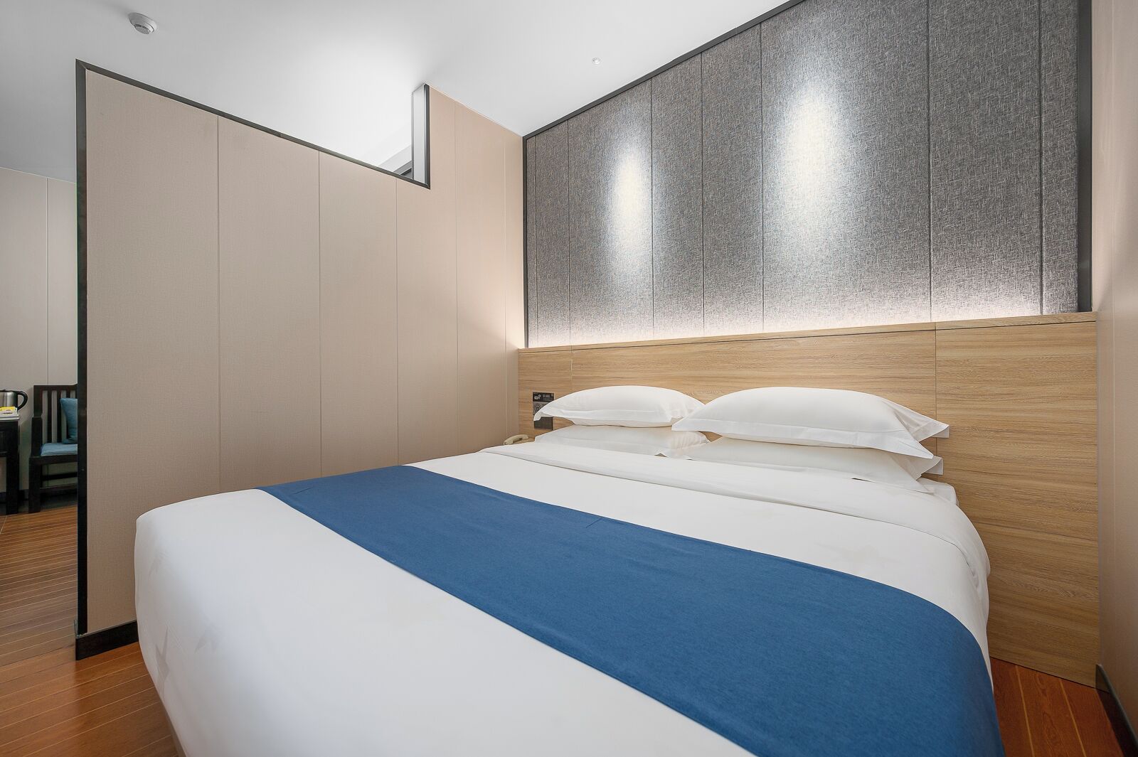 Ein modernes Hotelzimmer mit einem großen Bett, einem hölzernen Kopfteil und einem Kleiderschrank.