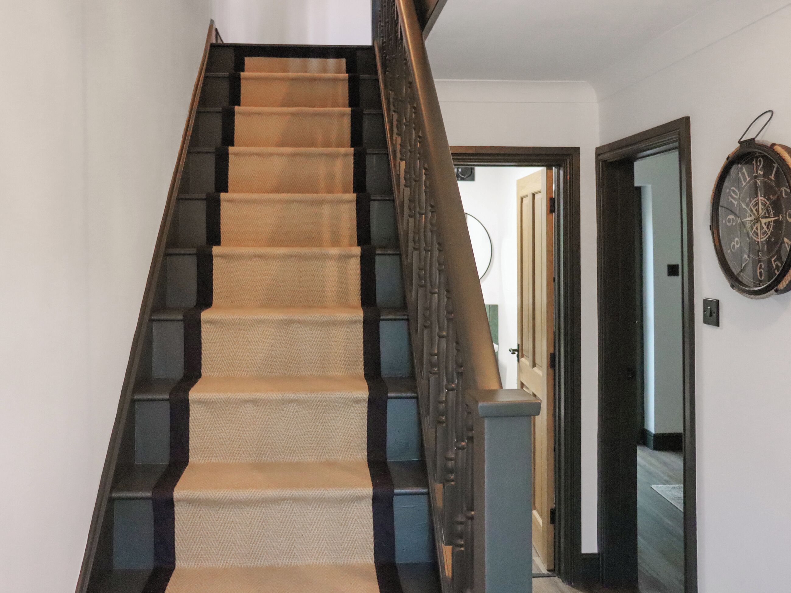 A carpeted staircase with a handrail, leading to a door with a wall-mounted clock.