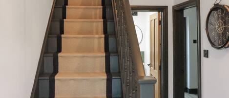 A carpeted staircase with a handrail, leading to a door with a wall-mounted clock.