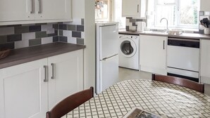A modern kitchen with white cabinets, a built-in washing machine, and a tiled backsplash. - 2 bedroom accommodation in Clun (Clun)
