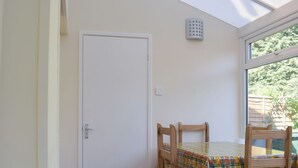 A room with a white door, a window with a view of greenery, and a table with a plaid tablecloth and wooden chairs. - 2 bedroom accommodation in Clun (Clun)