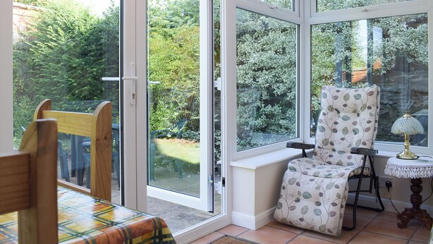 A conservatory with a table and chairs, a chair with a leaf pattern, and a lamp on a small table. - 2 bedroom accommodation in Clun (Clun)