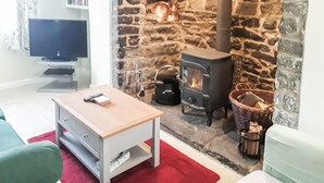 A cozy living room with a stone fireplace, a television, and a wooden table. - 2 bedroom accommodation in Clun (Clun)