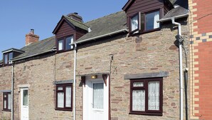 A row of stone houses with a uniform facade, featuring a central door and windows with dark frames. - 2 bedroom accommodation in Clun (Clun)