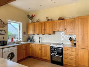 Eine Küche mit Holzausstattung, einer Waschmaschine, einem Backofen und einem Fenster mit Blick ins Freie.