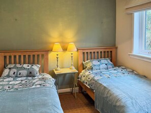 Ein Schlafzimmer mit zwei Einzelbetten, einem Nachttisch mit zwei Lampen und einem Fenster mit Jalousien.