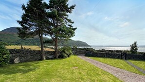 A grassy pathway leading to a stone wall with a gate, surrounded by trees and a view of the sea. - 3 bedroom accommodation in Lochranza (Lochranza)
