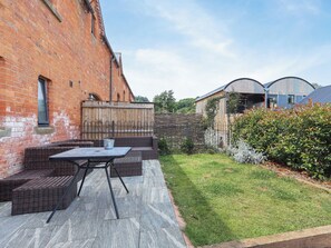 Een terras met rieten meubels en een tafel, een bakstenen muur en een gazon.