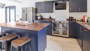 Una cocina moderna con armarios oscuros, una isla central con taburetes, horno empotrado y microondas.