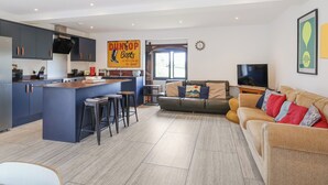 Una cocina moderna con una isla central, taburetes de bar, un sofá y un televisor en un espacio de sala con un amplio ventanal.