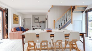 Una cocina moderna con una isla central, sillas blancas y una escalera que conduce a un nivel superior.