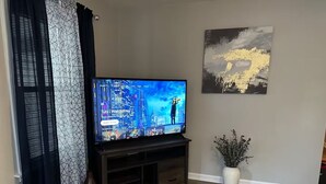 Ein Wohnzimmer mit Flachbildfernseher auf einem Holzboden, einer Vase mit getrockneten Blumen und einem Gemälde an der Wand.