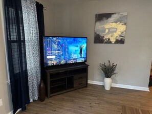 A living room with a flat-screen TV on a wooden stand, a vase with dried flowers, and a painting on the wall. - Chic Central Retreat (Evansville)